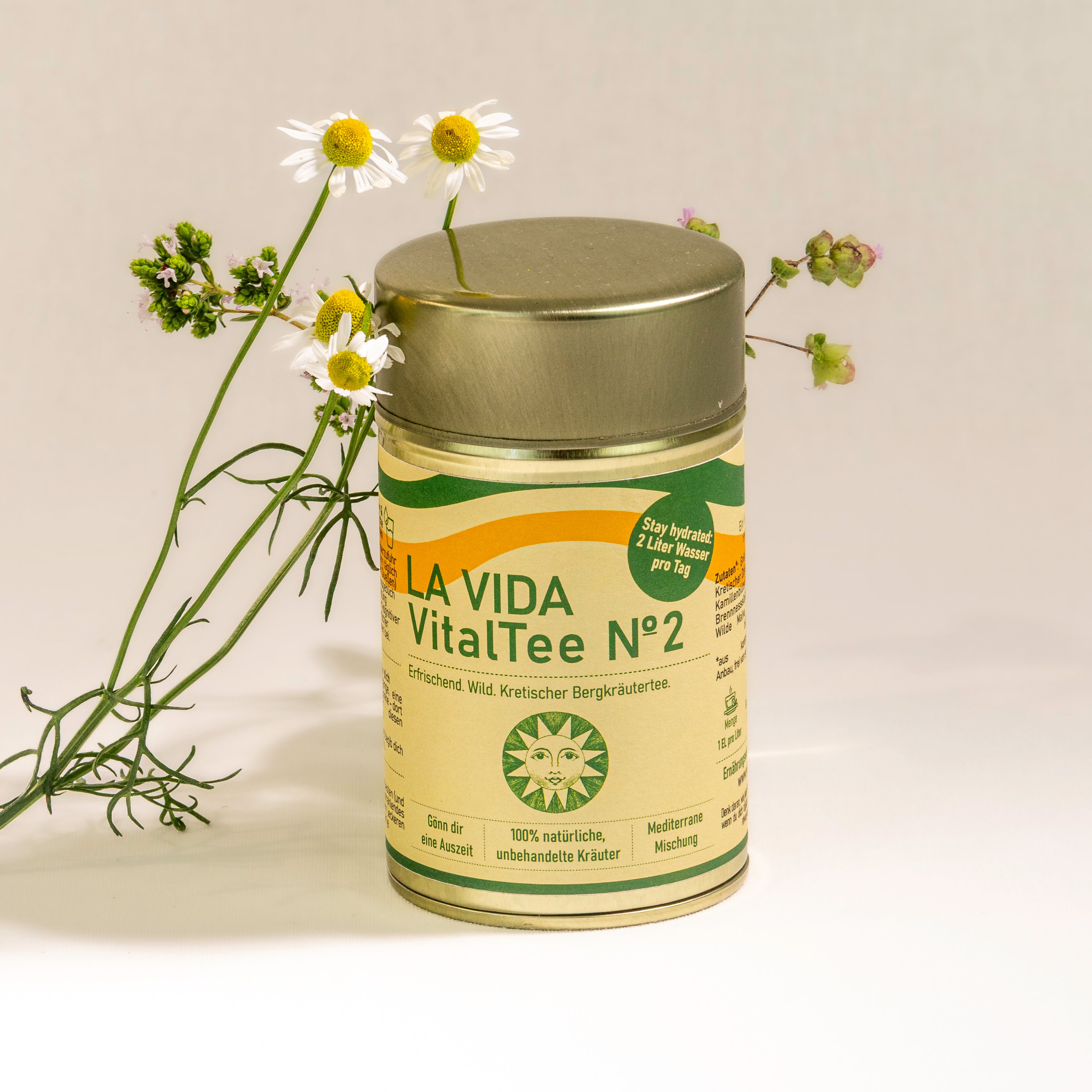 LA VIDA VitalTee No 2. Erfrischend wilde Kräutertee-Mischung aus wohlschmeckenden kretischen Bergkräutern wie Bergtee, Diptam und Minze zur täglichen Versorgung mit ausreichend Flüssigkeit. 45g in der goldenen Teedose. Frontansicht mit frischer Kamille, Oregano und Diptam.